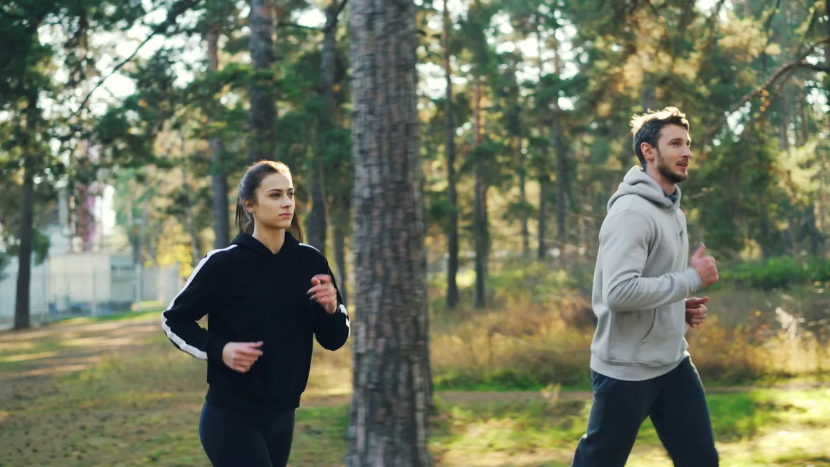 Two people running side by side along a forest path